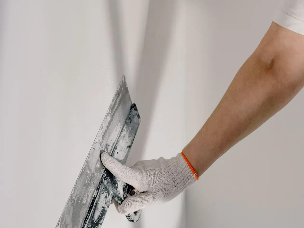 Hand mit Spachtel glättet eine Wand