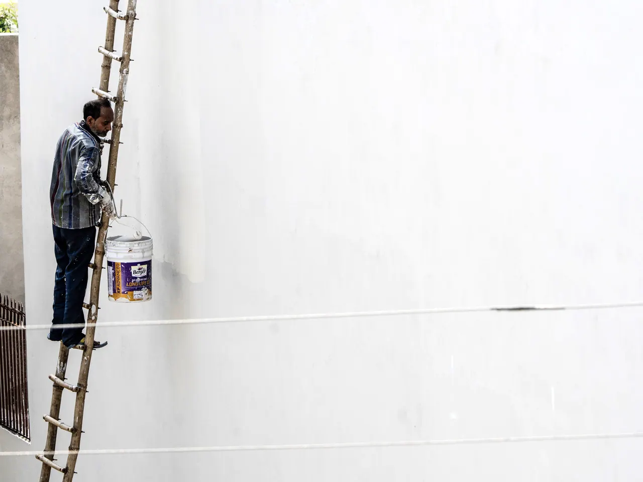 Maler auf einer Leiter streicht eine helle Hausfassade