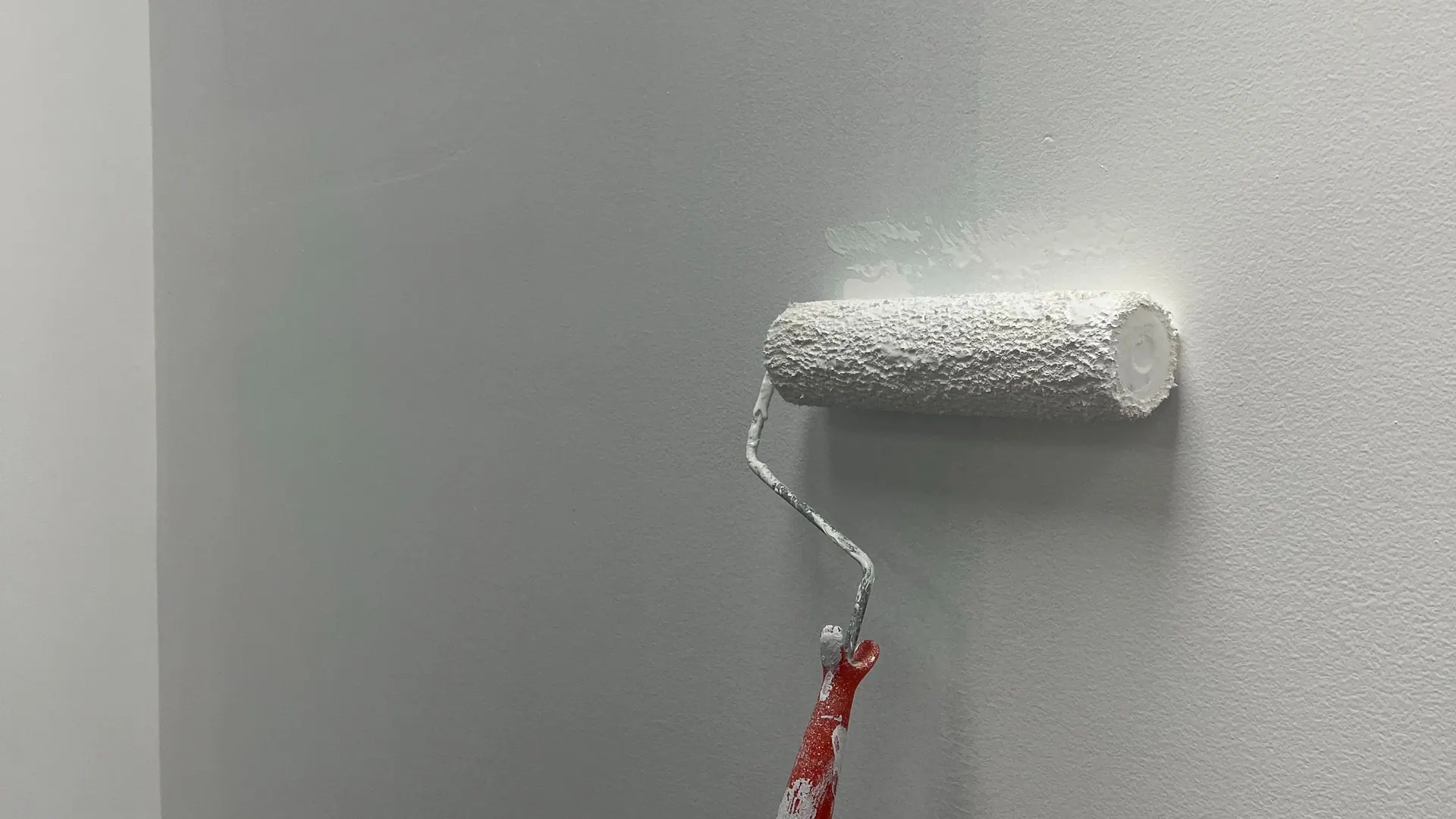 Farbrolle zieht frische weiße Farbe über eine Wand