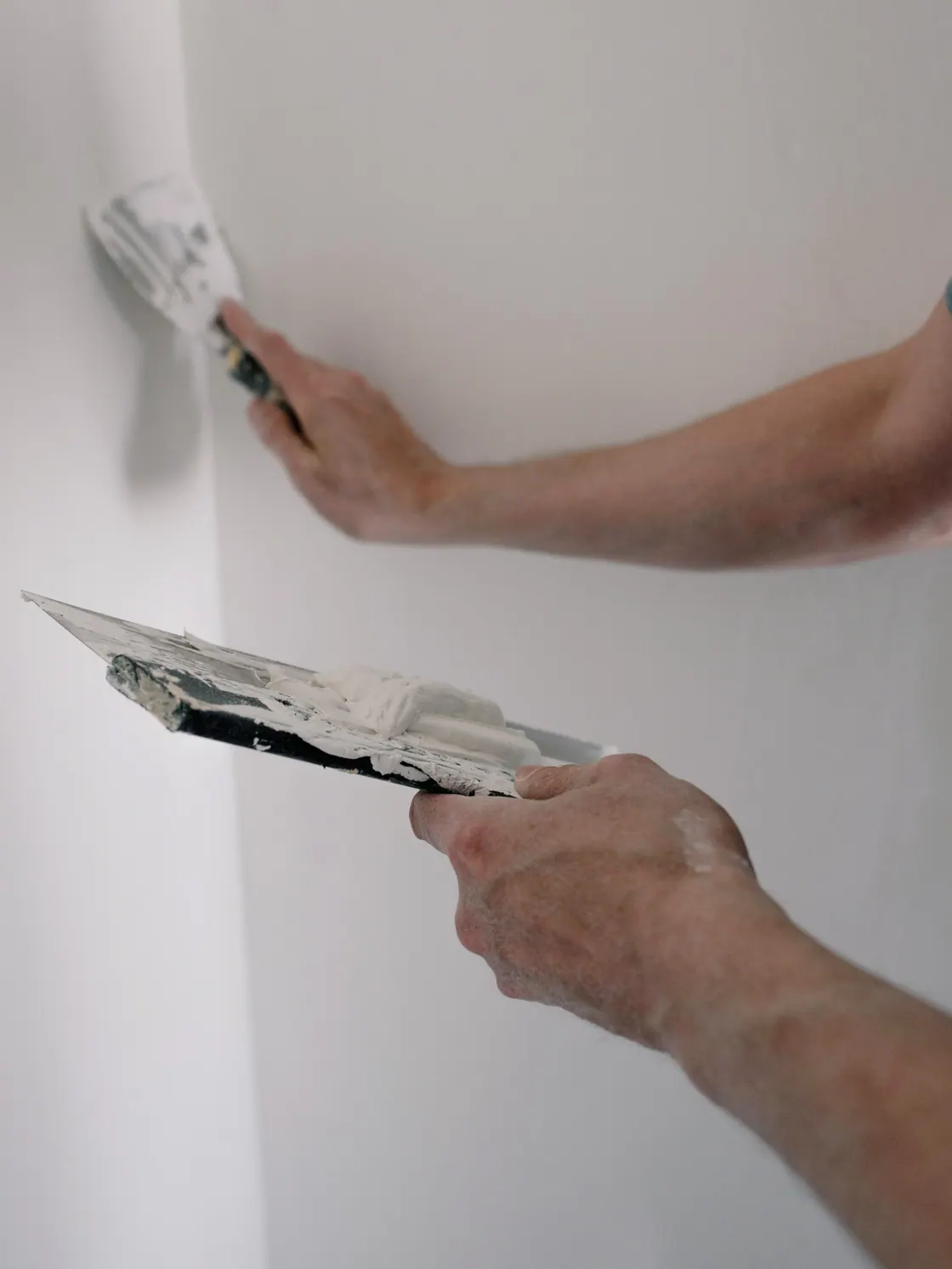 Hände des Malers mit Glättkelle und Spachtelmasse an einer Wand