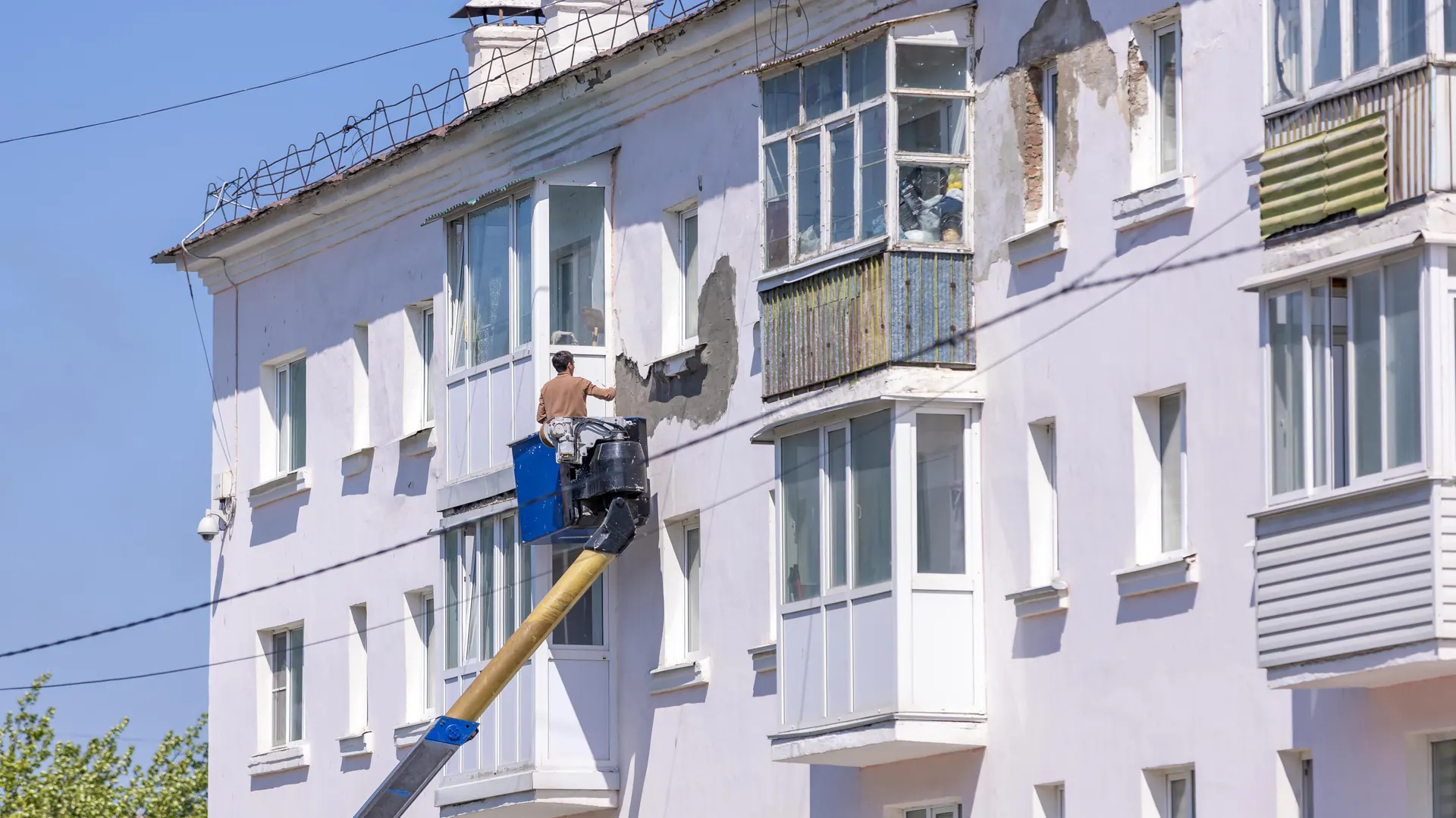 Fassade eines Mehrfamilienhauses wird von einer Hebebühne aus gestrichen